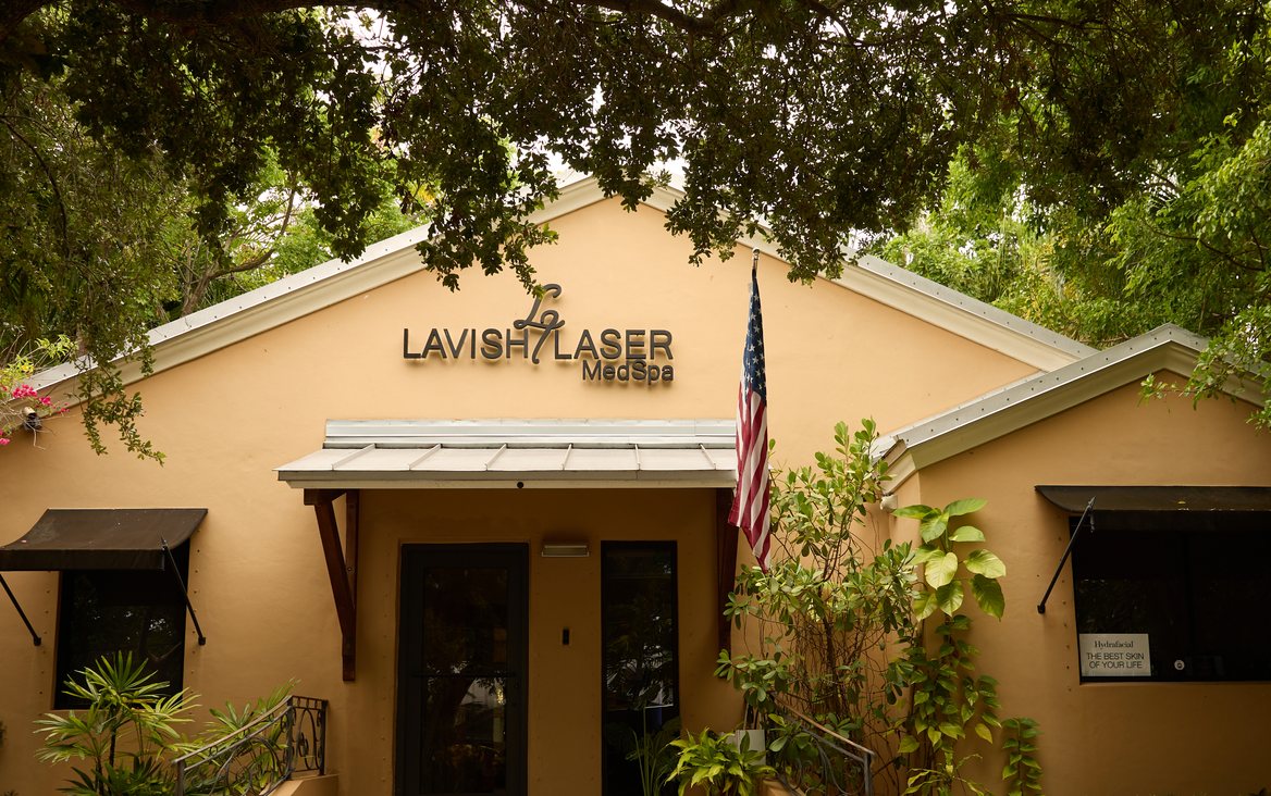 Lavish Laser MedSpa Coconut Grove storefront, a single-storey building under trees with an American flag by the entrance