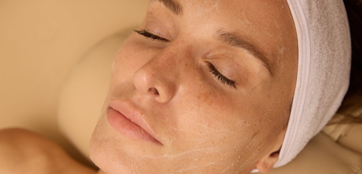 Relaxed client with a white headband lying back with eyes closed during a facial